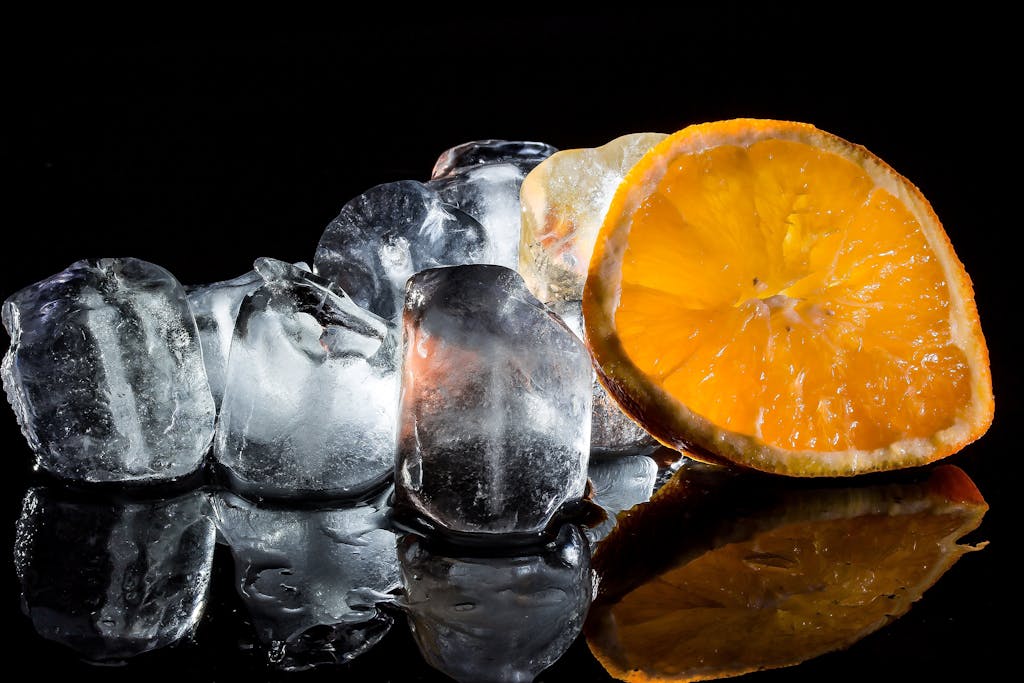 A vibrant still life of fresh orange slices and ice cubes against a dark background.