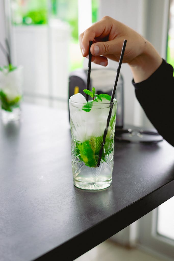 Hand stirring a refreshing mojito cocktail with mint and lime on a modern table.